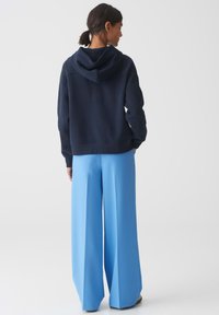 Felpa blu navy con cappuccio e vestibilità rilassata, abbinata a pantaloni a gamba larga azzurri, che mostrano una texture liscia.