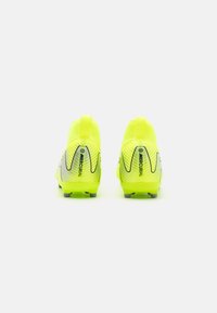 Des chaussures de football jaune vif présentent un design montante, une surface texturée et des accents noirs sur le talon avec un logo "MERCURIAL".