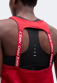 Dos d'une personne portant un soutien-gorge de sport noir sous un haut sans manches rouge avec des bretelles rouges Nike Pro sur les épaules.