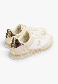 Baskets de sport beiges avec des accents scintillants dorés sur le talon, un logo de skull sur le côté, un tissu texturé et une semelle en caoutchouc légère.