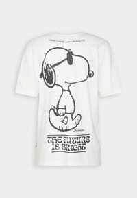 T-shirt en coton blanc présentant un grand graphisme noir de Snoopy avec le texte "L'AVENIR EST RADIEUX" en dessous, et "PRENEZ SOIN avec PEANUTS" au-dessus.