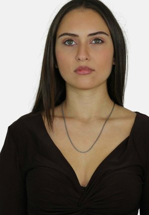 Collana in argento indossata da un modello, che mostra un design attorcigliato con una superficie liscia, abbinata a una maglietta marrone con scollo a V profondo.