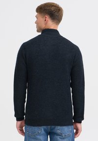 Donkere gebreide trui met een hoge kraag, gestructureerde stof en lange mouwen. Gecombineerd met lichtblauwe denim jeans.