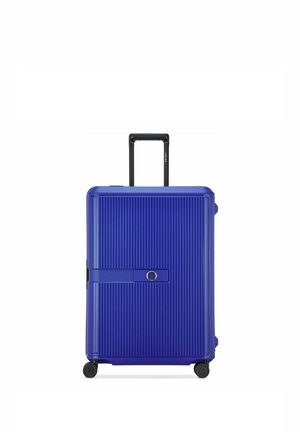Maleta grande de carcasa dura azul con estrías verticales, asa telescópica, cuatro ruedas y correa horizontal con cerradura circular en el centro.