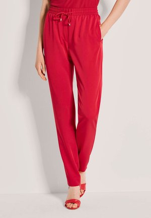 Rote Hosen mit elastischem Bund, seitlichen Taschen, schmal zulaufendem Bein und glatter Textur, ausgestattet mit einem Kordelzug und kombiniert mit passenden Sandalen.