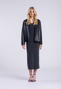Giacca corta in pelle nera sopra un lungo vestito grigio a coste. L'outfit presenta una silhouette aderente e sandali neri con tacco aperto.