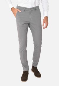 Pantaloni grigi slim-fit in cotone, con chiusura a bottone, tasche laterali e una superficie liscia, abbinati a scarpe in suede marroni.