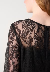Juoda nėriniuota suknelė su sudėtingais gėlių raštais, permatomomis tinklinėmis rankovėmis, tvirta liemeniu ir užtrauktuku nugaroje.
