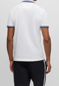 Polo blanc avec une finition texturée, doté d'un col à rayures bleues et de poignets à rayures bleues. Le dos présente une coupe nette sans détails supplémentaires.