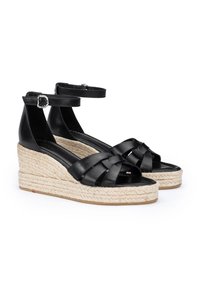 Sandales compensées en cuir noir avec une semelle intermédiaire en espadrille, présentant un design de lanières croisées et une lanière de cheville avec une boucle en argent.