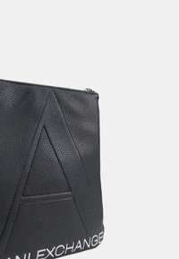 Borsa in pelle nera con superficie testurizzata, design angolare con una forma 'A' prominente e branding bianco "EXCHANGE" nella parte inferiore.