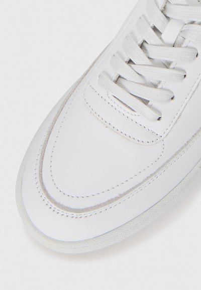 Sneaker bianco in pelle con suola testurizzata e lacci bianchi, che mostra cuciture dettagliate sulla punta e sulla parte superiore.