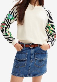 Krémový svetr se zebra vzorem na rukávech zdobený květinovými akcenty; spárováno s modrou denimovou sukní se cvočky na kapsách.