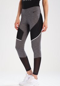 Legginsy z wysokim stanem wykonane z szarego materiału z czarnymi akcentami z siateczki. Charakteryzują się zaokrąglonym wzorem oraz białym wykończeniem wzdłuż szwów.