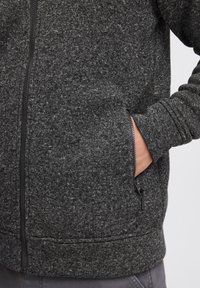 Dark gray zip-up sweatshirt with a textured fabric, visible side pockets, and a contrasting black zipper. Soft, casual design.