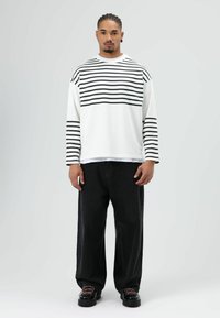 Wit shirt met lange mouwen en horizontale zwarte strepen; gecombineerd met loszittende zwarte broek en zwarte laarzen met roze veters.