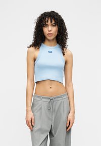 Ανοιχτό μπλε cropped τοπ με ριμπ υφή και στρογγυλή λαιμόκοψη, που διαθέτει μια μικρή μπλε ετικέτα μάρκας στο μπροστινό μέρος. Συνδυάζεται με γκρι παντελόνια.