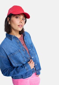 Jeansjacke mit lockerer Passform, hellblauer Farbe, zwei Brusttaschen und Knopfverschlüssen, kombiniert mit einem rot-weiß gestreiften Hemd und pinkfarbenen Cordhosen.