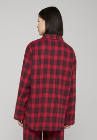 Chemise oversize à carreaux rouges et noirs, avec un col, des manches longues et une coupe décontractée. Tissu doux avec une texture lisse et un détail de couture au dos.