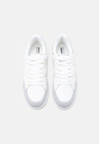 Ζευγάρι λευκά και ανοιχτό γκρι χαμηλά αθλητικά παπούτσια με κορδόνια, μαλακό επενδεδυμένο γιακά και αναπνεύσιμες διάτρητες μύτες σε λευκό φόντο.