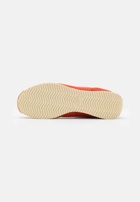 Red sneaker with a textured sole, featuring a herringbone pattern in cream. Upper material appears smooth with contrasting white accents.