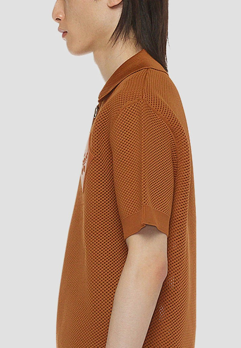 Braunes Polohemd aus Netzstoff mit kurzen Ärmeln, ausgestattet mit einem gerippten Kragen und einem Logopatch auf der Brust. Texturiertes Material und lockere Passform.