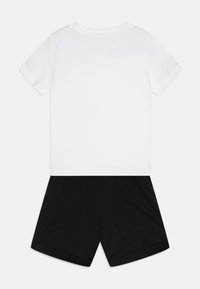 Biela bavlnená tričko s krátkymi rukávmi, spárované s čiernymi bavlnenými šortkami. Jednoduchý dizajn, bez vzorov alebo akcentov.