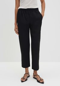 Zwarte, wijde broek met een elastische tailleband, zijvakken en een soepele textuur. Gecombineerd met zwarte sandalen met bandjes.