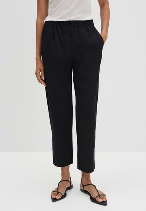 Schwarze, weit geschnittene Hosen mit elastischem Bund, Seitentaschen und glatter Textur. Kombiniert mit schwarzen Riemchen-Sandalen.
