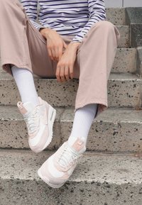 Baltas un rozā sporta apavi ar acs un ādas materiāliem, mīkstinātu apkakli un baltām zālēm. Valkāti ar gaiši rozā biksēm un baltām zeķēm.