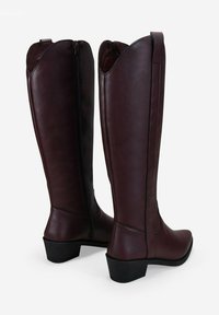 Botas altas de cuero burdeos con un acabado suave, punta afilada y tacón bajo y grueso. Presentan una cremallera en la parte trasera y bordes superiores con forma de ondas.