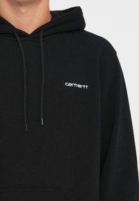 Black hoodie with a drawstring hood, front pocket, and white embroidered logo on the left chest, made from soft, textured fabric.