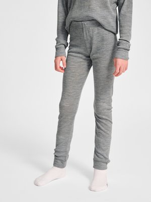 Barn iført tætsiddende grå svedundertøj bukser og matchende top, stående barfodet mod en ensfarvet baggrund.