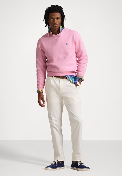 Pink sweater, hvide bukser og blå sko. Sweateren har en tynd krave, fremvist over en flerfarvet ternet skjorte. Afslappet stil.