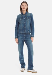 Denim jacket in medium blue, featuring a collared neckline, front pockets, and button closures. Paired with matching blue denim jeans.