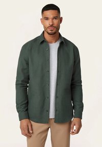 Groene button-up shirt van een zachte stof, met een kraag, zwarte knopen en lange mouwen, gelaagd over een lichtgrijs T-shirt.