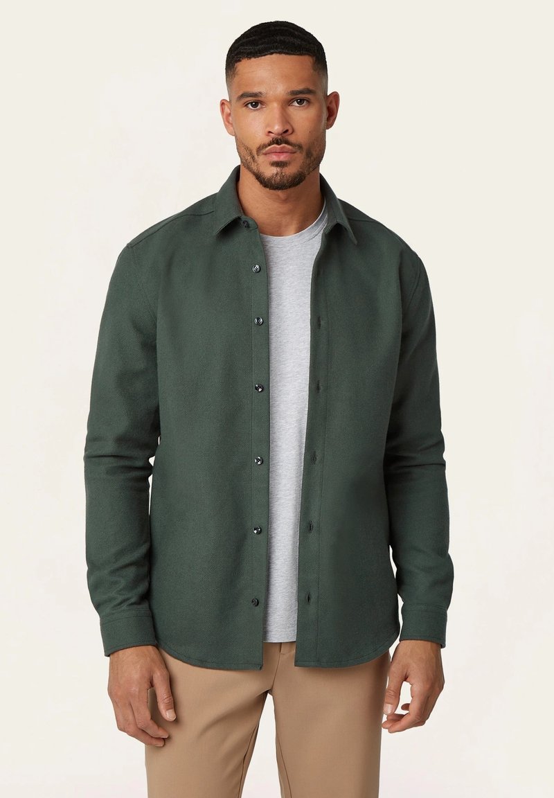 Groene button-up shirt van een zachte stof, met een kraag, zwarte knopen en lange mouwen, gelaagd over een lichtgrijs T-shirt.