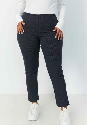 Pantalons noirs à rayures avec une coupe ajustée, dotés d'une taille haute et de poches latérales, associés à des baskets blanches. Texture de tissu lisse.
