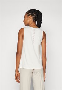Letvægts, ærmeløs cremefarvet tanktop med en glat tekstur, der har teksten "STATE OF MIND" trykt lodret i lys pink på ryggen.