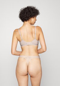 Beige beha met verstelbare bandjes, haaksluiting en een soepele stof. Gecombineerd met een bijpassende string die minimale bedekking biedt en een zachte textuur heeft.