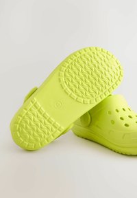 Lime zöld klumpák texturált talppal, vízelvezető lyukakkal a felső részen és széles pánttal a biztonságos illeszkedés érdekében. Könnyűek és tartós anyagból készültek.