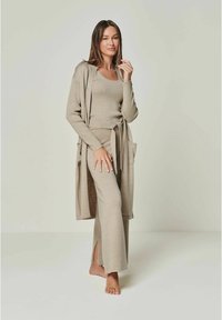 Beige Strick-Loungewear-Set mit einer langen Strickjacke mit Taschen, einem taillierten Oberteil und weit geschnittenen Hosen mit Seitenschlitzen. Weiche Textur.