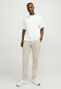 Camiseta blanca de manga corta, pantalones beige a medida y zapatillas deportivas blancas. El tejido parece suave, con un corte relajado y sutiles detalles de costura.