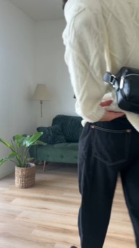 Fekete, laza szabású nadrág fehér varrási részletekkel, egy krémszínű, texturált kötött pulóverrel és egy kis fekete keresztpántos táskával kombinálva.