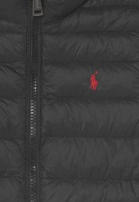 Černá prošívaná péřová bunda s prošívanou strukturou, vybavená zipovým uzávěrem a malým červeným vyšitým logem na levé straně hrudníku.