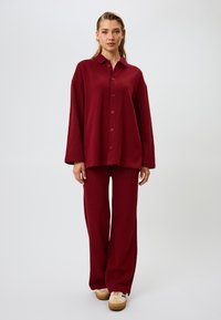 Bordeaux gebreid loungewear set met een oversized overhemd met knopen en wijde broekspijpen, met een zachte textuur en eenvoudig ontwerp.
