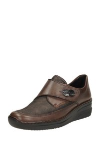 Zapato marrón de piel sin cordones con un panel de tela texturizada de tono más oscuro, acentos de botones decorativos y una suela de cuña baja para mayor comodidad.