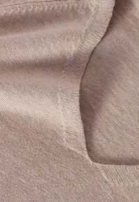 Jasnobeżowa tkanina o miękkiej fakturze z delikatnym melanżowym wzorem. Prezentuje detal dekoltu oraz drobne przeszycia wzdłuż krawędzi.