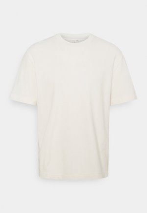 Prosty biały t-shirt z krótkim rękawem i okrągłym dekoltem, o luźnym kroju, prezentowany na jasnoszarym tle.