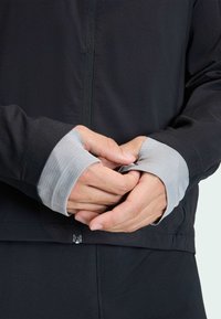 Black athletic jacket with a front zip, featuring gray thumbhole cuffs and a smooth texture; minimalistic design with no patterns.